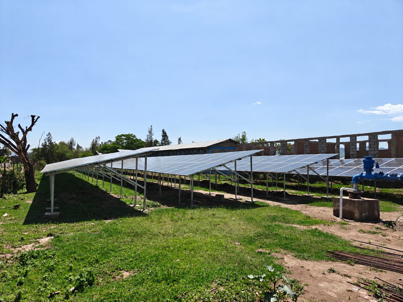 Ground-mounted solar array beside a borehole wellhead at a solar water pumping site